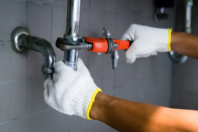 Eine Person mit weißen Handschuhen befestigt mit einem roten Schraubenschlüssel ein glänzendes Metallrohr an einer gefliesten Wand und vermittelt dabei Konzentration und Präzision.